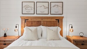 A neatly made bed with a wooden headboard, two bedside tables with lamps, and three framed pictures of mountains labeled South Sister, Middle Sister, and North Sister. - Steps to Village, A/C, Hot Tub, 6 SHARC, Bikes (Sunriver)