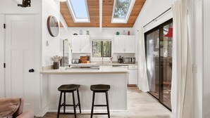 A modern kitchen with a central island, skylights, and a sliding glass door leading to an outdoor area. - Steps to Village, A/C, Hot Tub, 6 SHARC, Bikes (Sunriver)