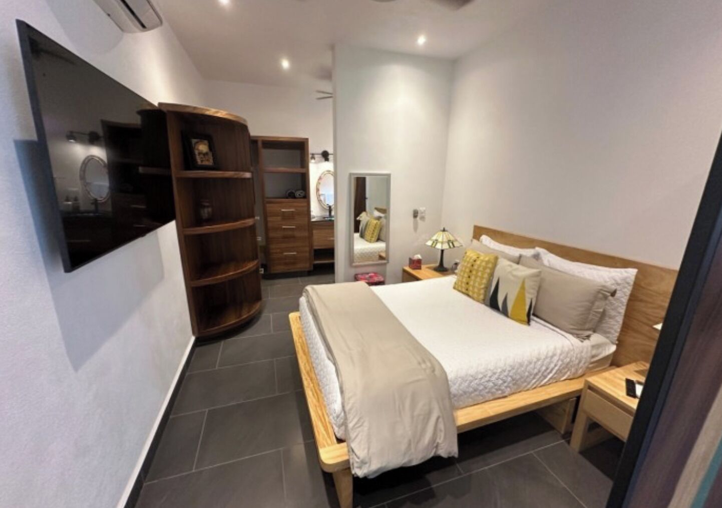 A bedroom with a bed, bedside table, lamp, wardrobe, and a TV mounted on the wall.