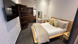 Ein Schlafzimmer mit Bett, Nachttisch, Lampe, Kleiderschrank und einem an der Wand befestigten Fernseher.