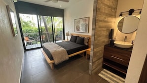 Ein modernes Schlafzimmer mit Bett, ein Badezimmer mit Waschbecken und Spiegel sowie ein Balkon mit einem Stuhl.