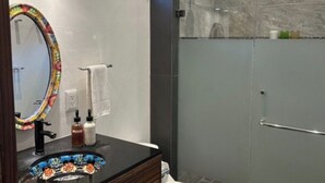 Ein Badezimmer mit modernem Design, das eine gläserne Dusche, ein Waschbecken mit farbenfrohem Fliesenbecken und einen Spiegel mit dekorativem Rahmen zeigt.