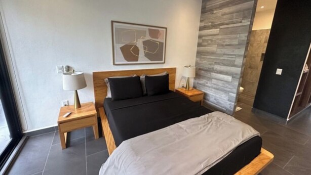 Et moderne hotelværelse med en stor seng, to sengeborde med lamper, en træsenggavl og et stort abstrakt maleri på væggen.