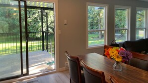 A dining area with a table and chairs, a vase of flowers, and a view of a green outdoor space through a sliding glass door. - Superb 3-bedroom farmhouse in Abbotsford (Abbotsford)
