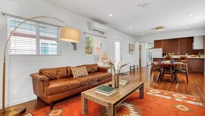 Een moderne woonkamer met een leren bank, een houten salontafel en een eethoek met een houten tafel en stoelen.