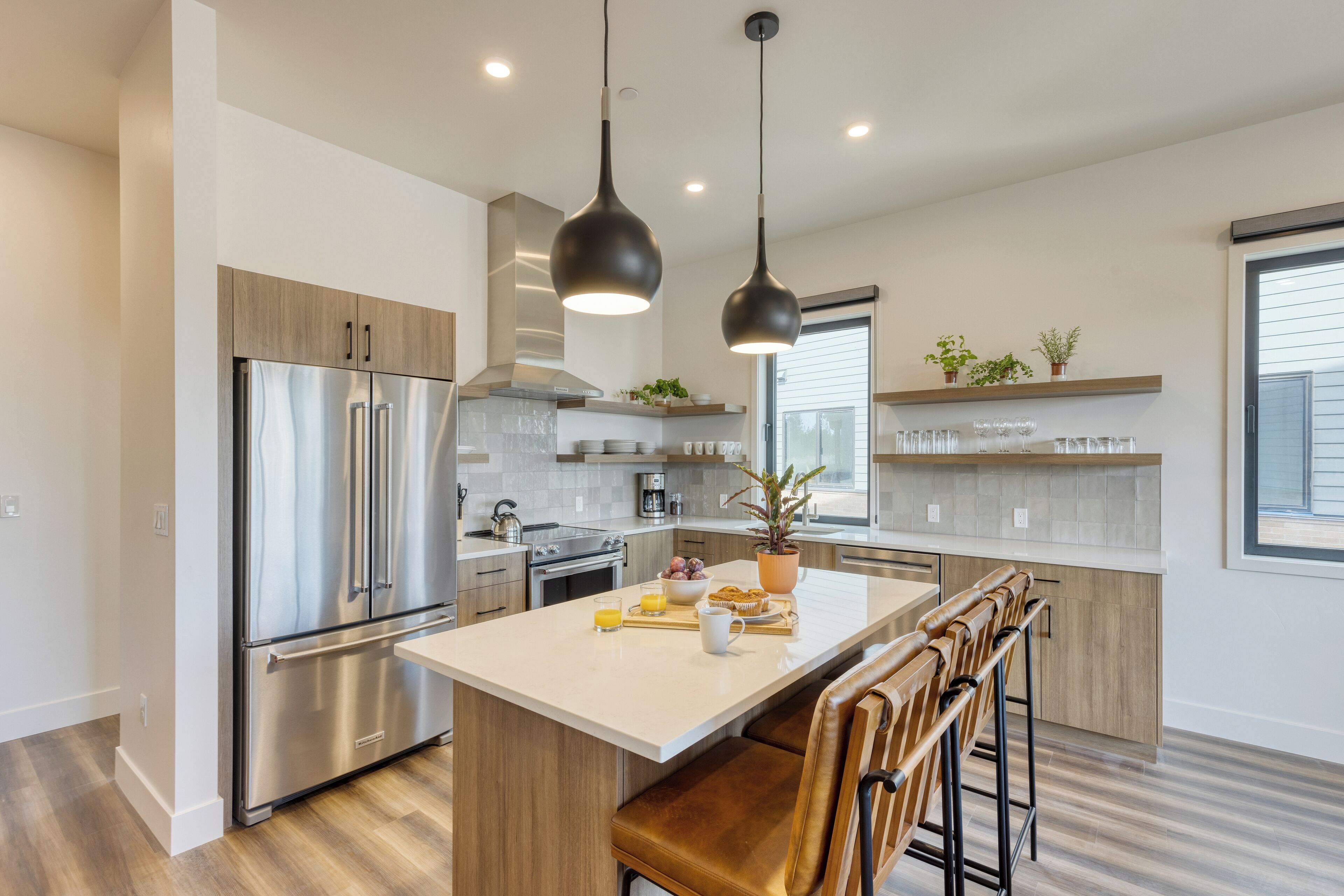 Een moderne keuken met roestvrijstalen apparatuur, een centraal eiland met barkrukken, hanglampen en een raam met zonwering.