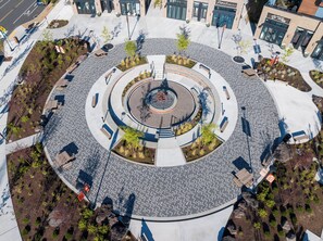 A circular plaza with seating areas, a central fountain, and surrounding greenery.