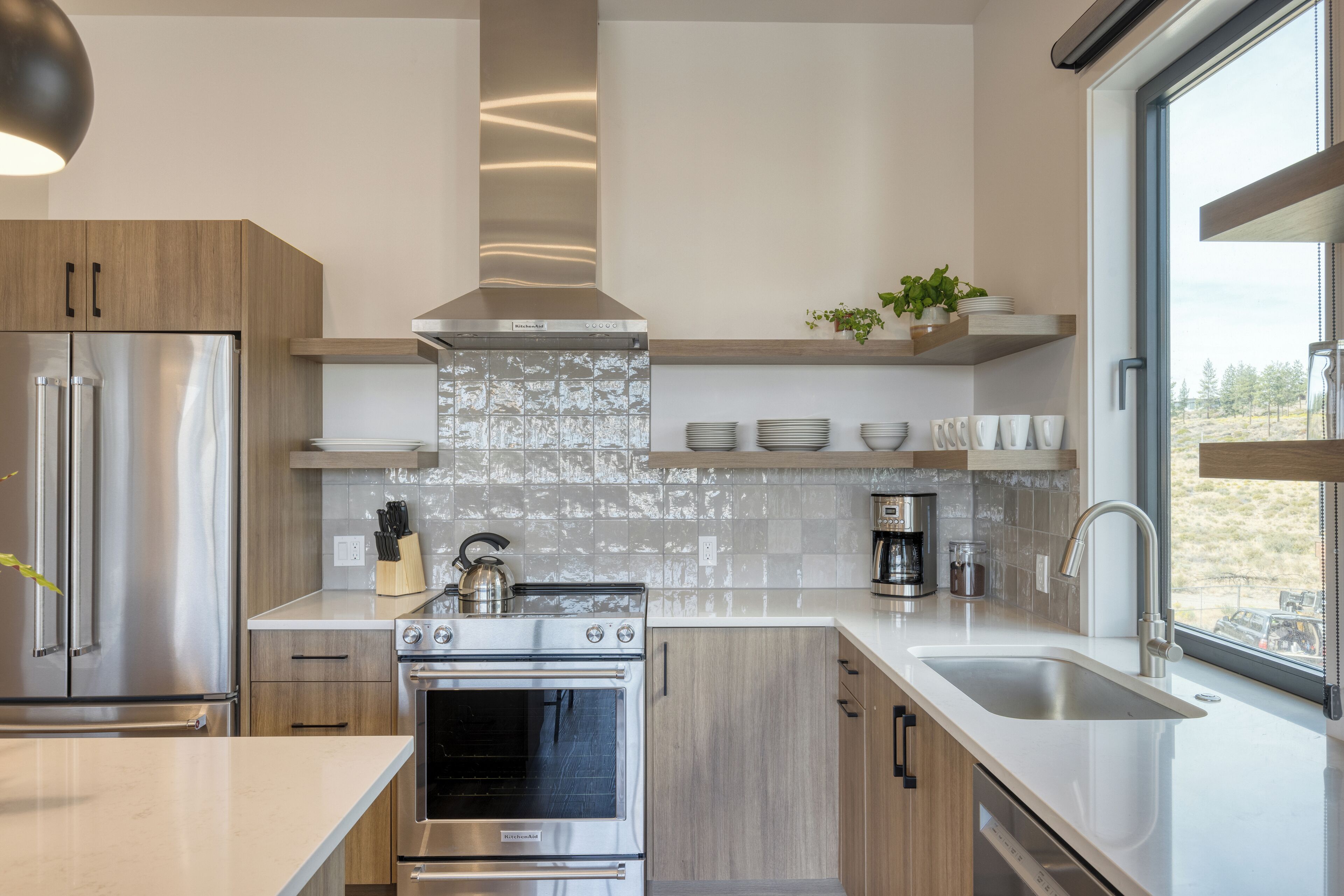 Une cuisine moderne dotée d’appareils électroménagers en acier inoxydable, de meubles en bois et d’une grande fenêtre offrant une vue dégagée.
