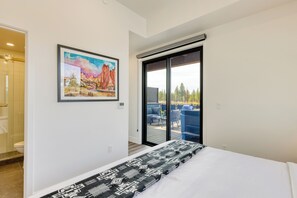 A bedroom with a bed, a sliding glass door to a balcony, and a painting on the wall.