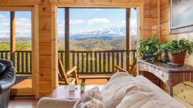 A wooden cabin with a balcony, a bed, a table, and a view of snow-capped mountains.