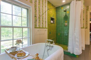 A bathroom with a bathtub, shower, and a window with a view of greenery.