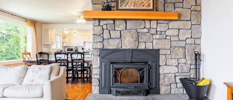 A cozy living room with a stone fireplace, a sofa, and a dining area in the background.