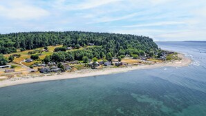 Una vista aerea di una zona residenziale costiera con case, una spiaggia e una collina ricoperta di boschi.