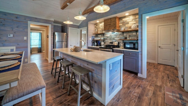 A modern kitchen with a large island, bar stools, and a dining area with a wooden table and chairs. - Aloha Ohana by AvantStay | Private Pool Near Beach (Port Aransas)