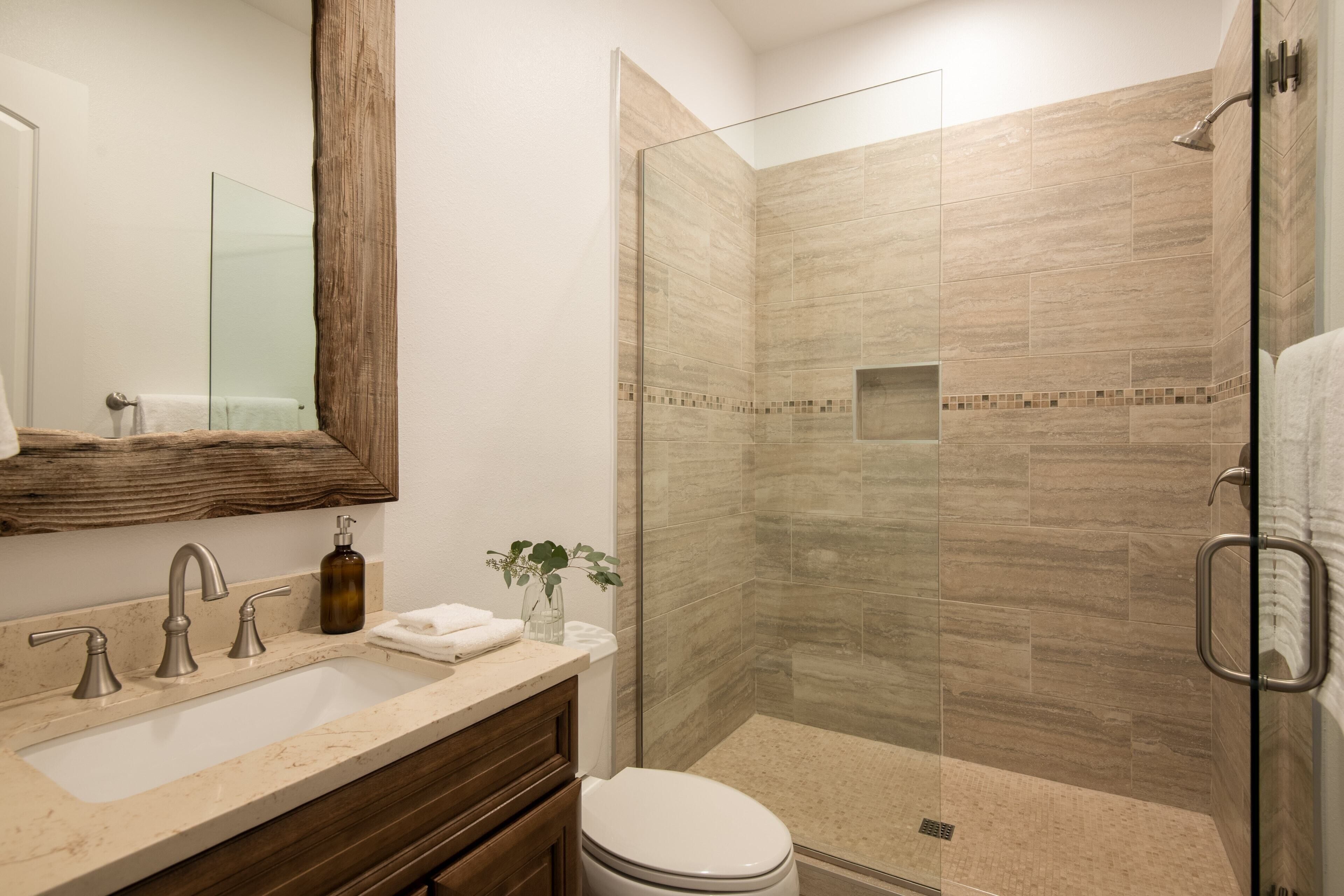 A modern bathroom with a glass-enclosed shower, a beige marble sink, and a wooden vanity.