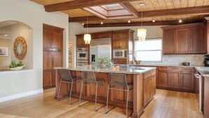 A spacious kitchen with wooden cabinets, a large island with bar stools, stainless steel appliances, and a skylight. - Wavebreak by AvantStay | Close to Beaches/Surfing (Solana Beach)