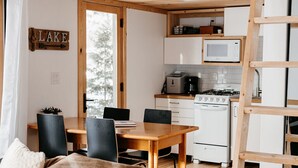 Et loftværelse med køjeseng i træ, et spiseområde med bord og stole, et køkken med komfur og mikroovn, samt et skilt der står 'LAKE'.