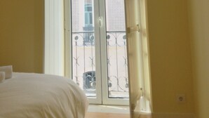 Een kamer met een bed, een raam met uitzicht op een gebouw, en een deur.