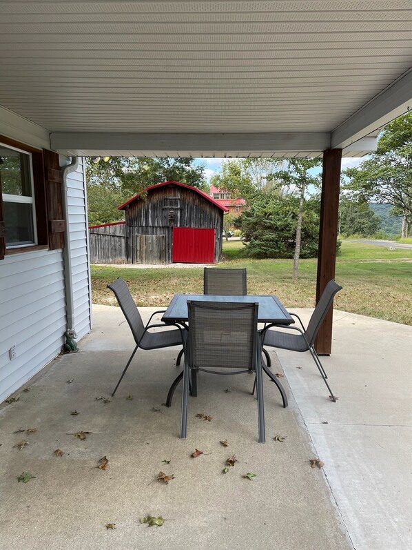A covered patio with a table and chairs, a red barn in the background, and a grassy yard. - Oxbow Overlook: Ohio River Bend Views, Private Pond, Pets Welcome (Magnet)