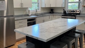 A modern kitchen with white cabinets, a large marble island, stainless steel appliances, and bar stools. - Oxbow Overlook: Ohio River Bend Views, Private Pond, Pets Welcome (Magnet)