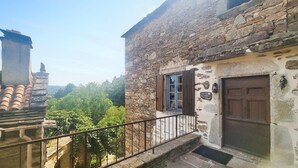 Un bâtiment en pierre avec une porte et des volets en bois, un petit balcon doté d’une rambarde en métal et un mur en pierre surmonté d’une lanterne.