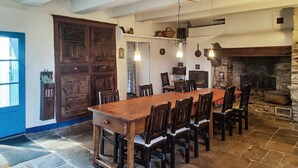 Un espace repas avec une longue table et des chaises en bois, une cheminée en pierre et une grande porte en bois.