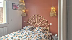 Une chambre à coucher avec une couvre-lit à motifs floraux, une tête de lit en bois et deux lampes suspendues.