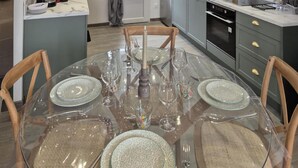 Une table ronde en verre, dressée pour quatre personnes, avec de la vaisselle et des verres transparents, entourée de chaises en bois.