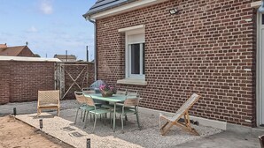 Une maison en briques avec un patio comprenant une table et des chaises, une fenêtre et une porte.