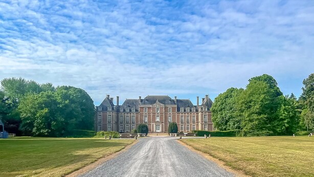 Un grand bâtiment historique à la façade symétrique, doté d’une entrée centrale et d’une pelouse bien entretenue à l’avant.