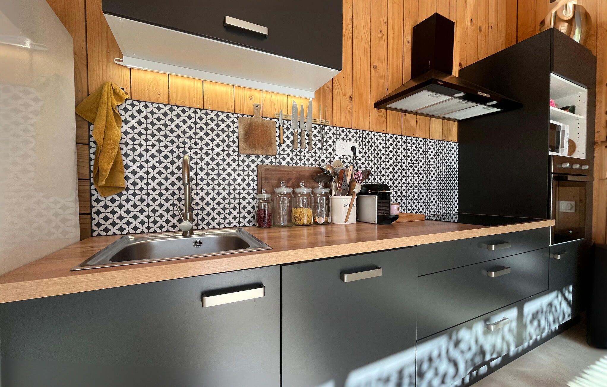 A modern kitchen with a black and white patterned backsplash, stainless steel sink, and wooden cabinets.