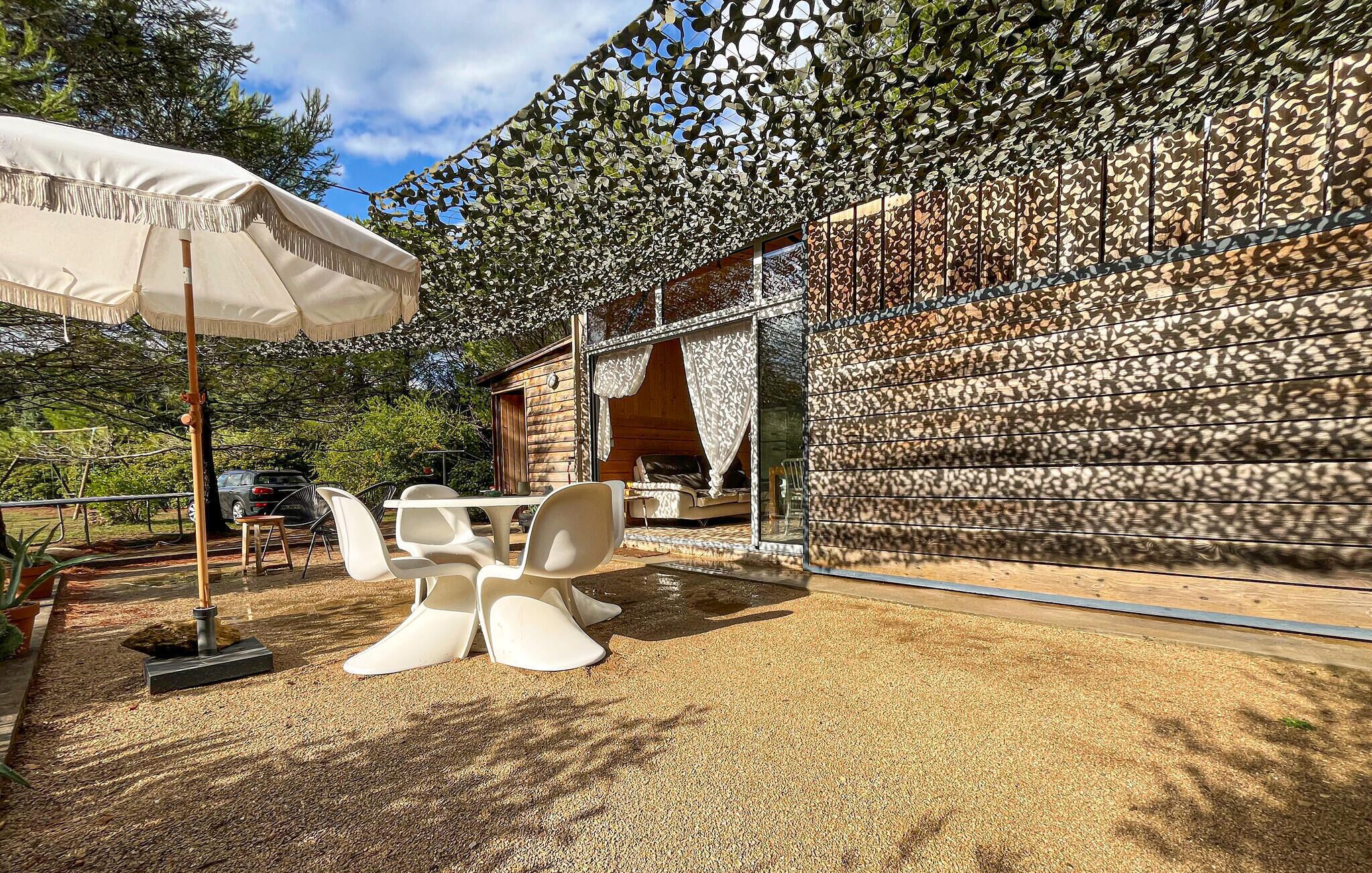 An outdoor seating area with a table and chairs, a white umbrella, and a decorative wall with a leaf pattern.