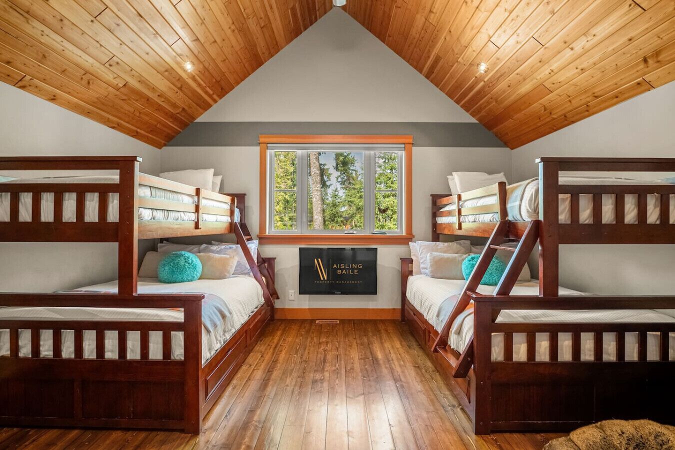Une chambre avec deux lits superposés, un plafond en bois, une fenêtre donnant sur les arbres et un panneau accroché au mur.