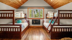 A bedroom with two bunk beds, wooden ceiling, a window with a view of trees, and a sign on the wall.