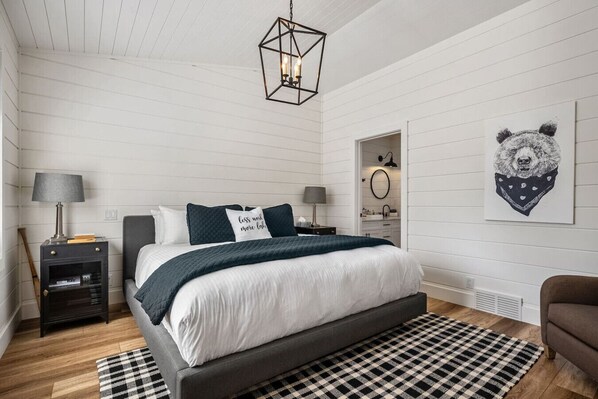 A modern bedroom with a bed, bedside tables, a hanging light fixture, a checkered rug, and a wall-mounted artwork.
