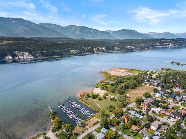 Vista aérea de una comunidad junto al lago con edificios residenciales, un puerto deportivo y montañas al fondo.