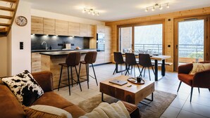 A modern kitchen with wooden cabinets, a dining area with a table and chairs, a sofa with a cowhide pillow, and a staircase. - Loft Petit Charbel - Charming stay with balconies - OVO Network (Châtel)