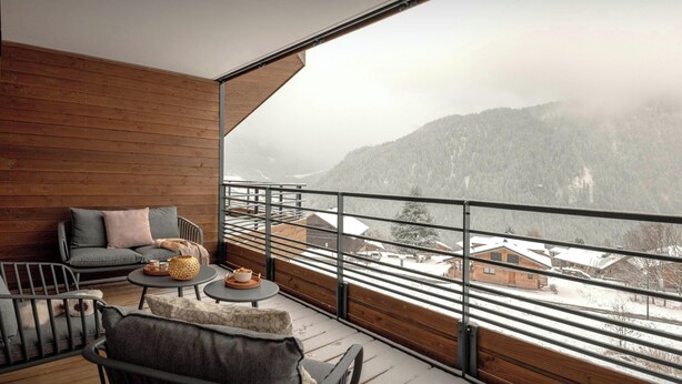 A balcony with a wooden floor, a sofa, a small table with a basket and a cup, and a view of a snowy mountain landscape. - Loft Petit Charbel - Charming stay with balconies - OVO Network (Châtel)