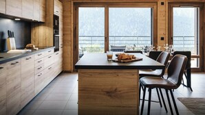 A modern kitchen with wooden cabinets, a central island, and a dining area with a view of the outdoors. - Loft Petit Charbel - Charming stay with balconies - OVO Network (Châtel)