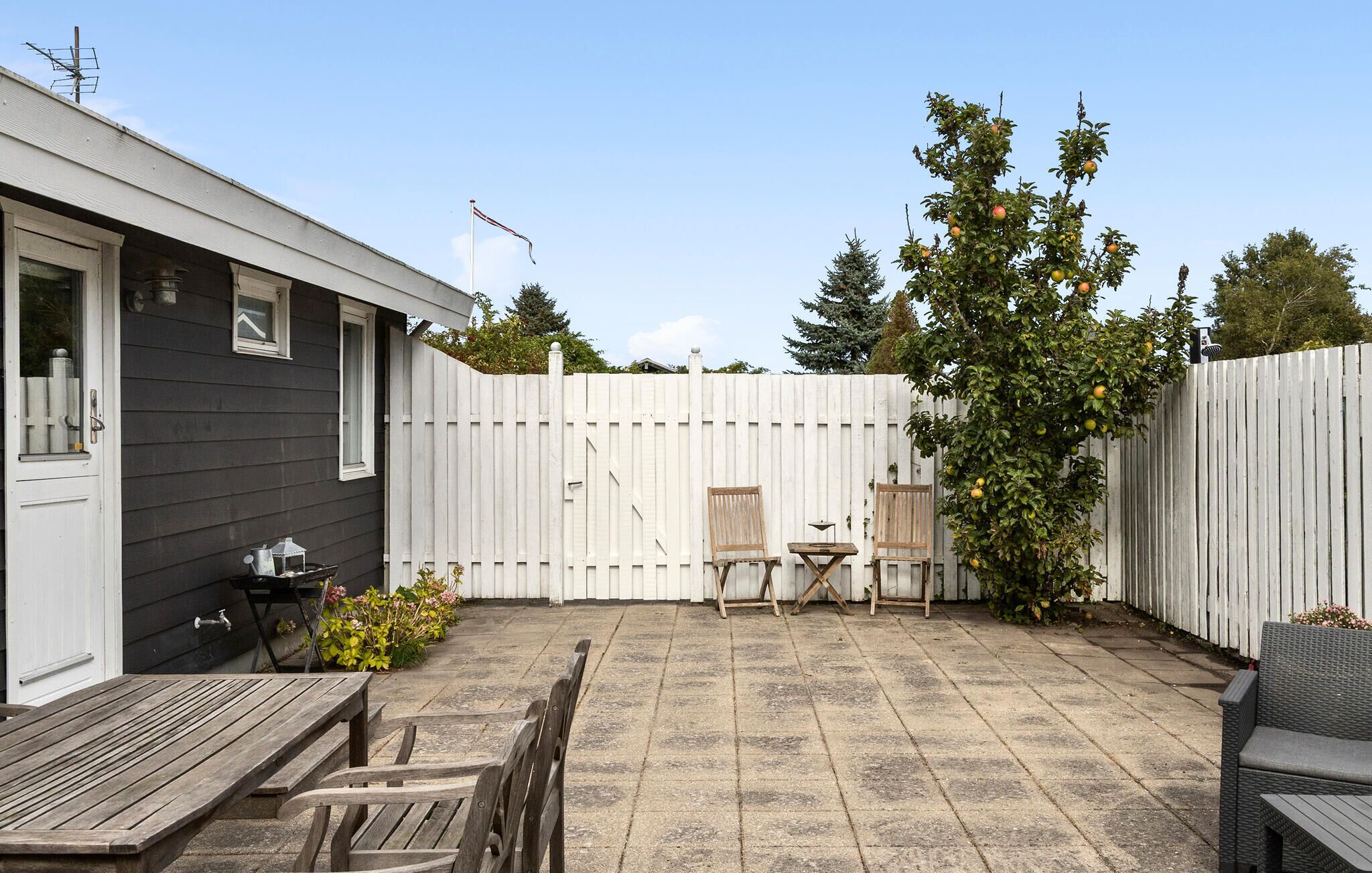 A patio with a table and chairs, a wooden fence, and a tree with fruit.