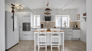 Moderni keittiö, jossa on valkoiset kaapit, keskellä sijaitseva saareke tuoleineen, sisäänrakennettu uuni ja suuri ikkuna, josta tulee runsaasti luonnonvaloa.