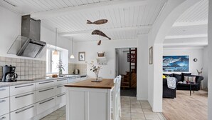 Moderni keittiö, jossa on valkoiset kaapit, puinen keittiösaareke ja ruokailutila, jossa on tumma sohva ja kalakuva.