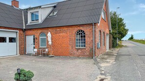Un bâtiment à deux étages, construit en briques, avec un toit en pente, un garage et un petit espace extérieur aménagé avec des chaises et une table.