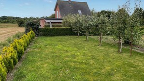 Une maison avec un toit en pente, entourée d’une pelouse bien entretenue et d’une haie.