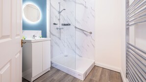 A bathroom with a glass-enclosed shower, a white vanity with a mirror, and a white door. - The Bell Hotel  (Burgh le Marsh)