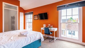 A hotel room with a bed, a desk, a chair, a TV, and a window with a view of buildings. - The Bell Hotel  (Burgh le Marsh)