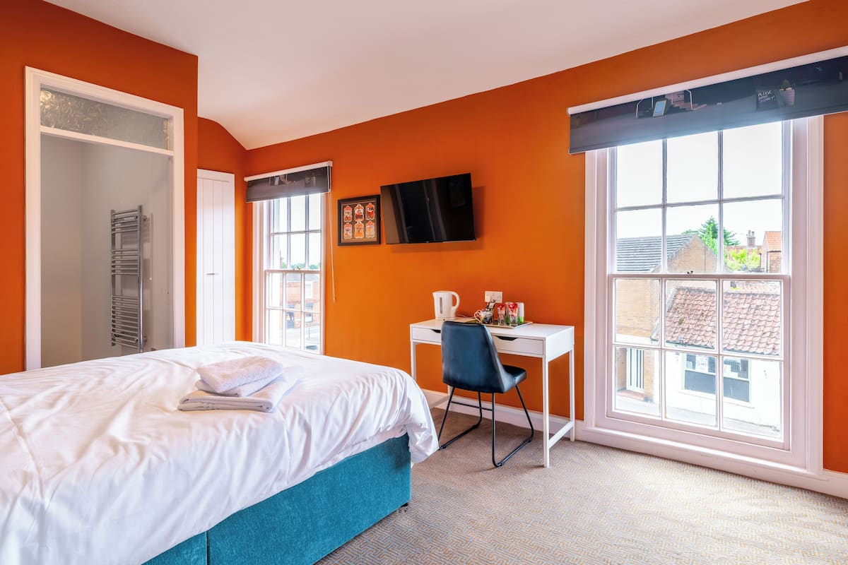 Habitación de hotel con cama, escritorio, silla, televisor y ventana con vistas a edificios.