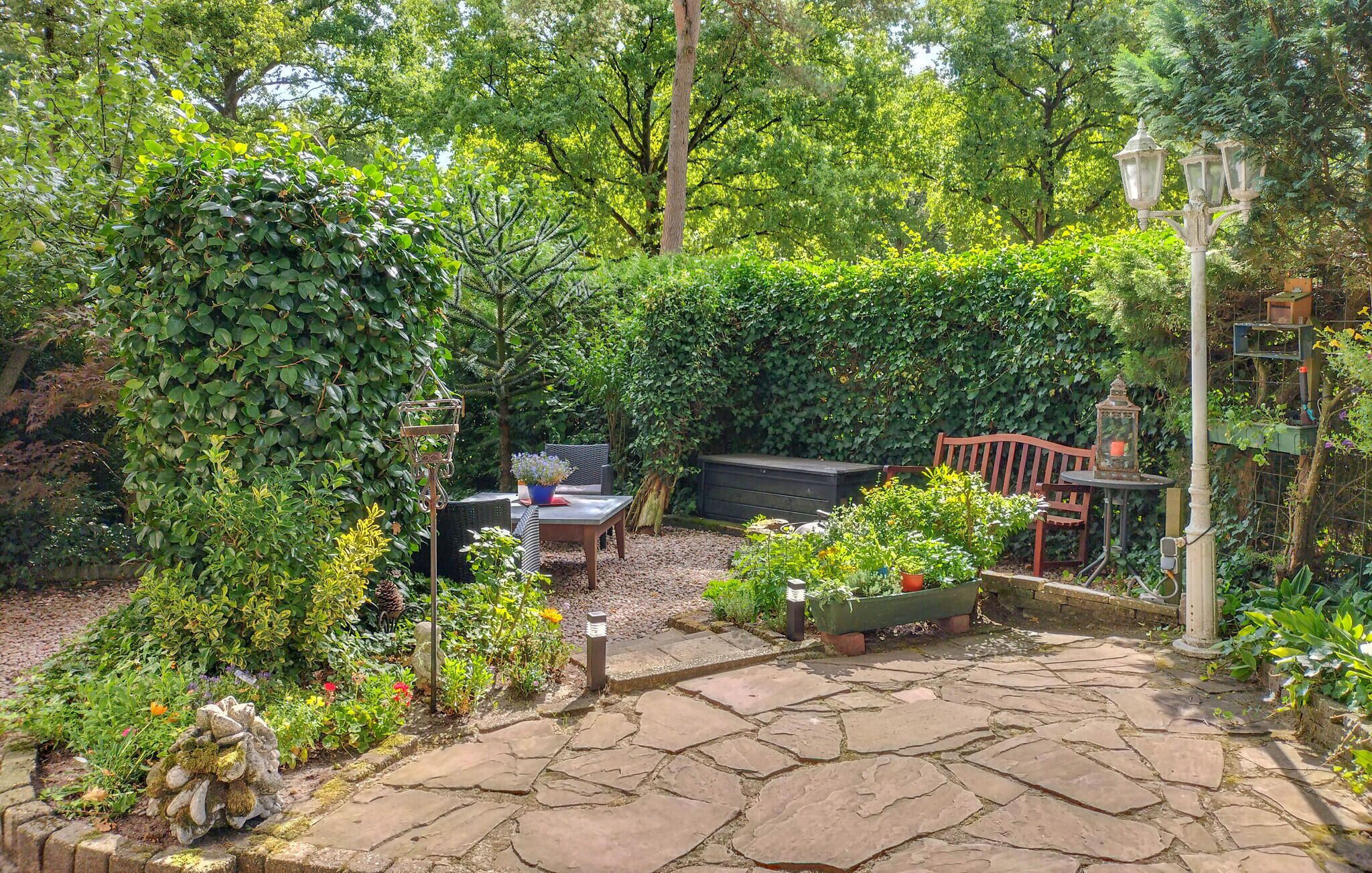 A garden patio with stone flooring, a wooden bench, a table with chairs, and a variety of potted plants.