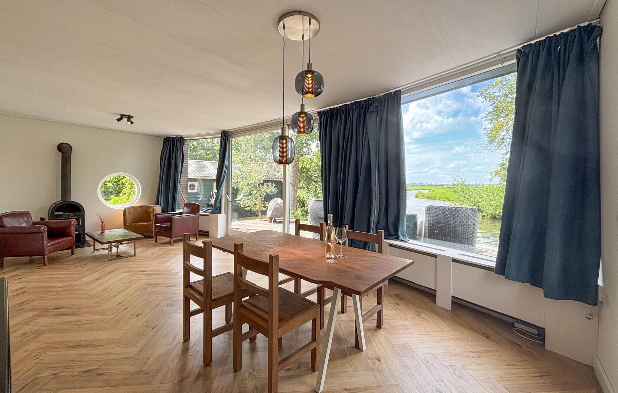 A spacious room with a wooden dining table, chairs, a sofa, and a large window with curtains.