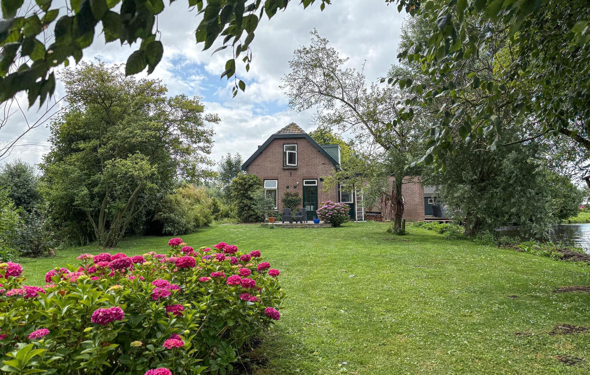 A house with a sloped roof, surrounded by a well-maintained lawn and flowering plants.